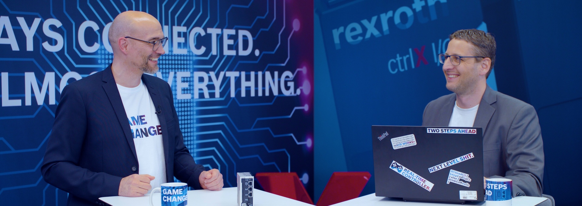 Host Christian Zentraf and his guest Kai Müller stand at meeting tables and talk about configuring a handling application with ctrlX CORE, the control hardware of the automation solution ctrlX AUTOMATION