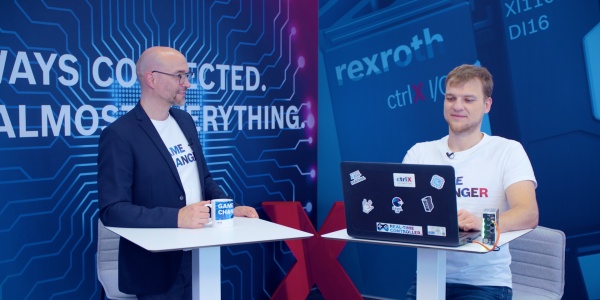 Gastgeber Christian Zentraf und sein Gast Michael Schäfer stehen an Besprechungstischen und sprechen über das Programmieren von Python-Skripten direkt auf der ctrlX CORE, der Steuerungshardware der Automatisierungslösung ctrlX AUTOMATION