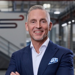 Portrait of a man who stands inside a production building, the background is slightly blurred.