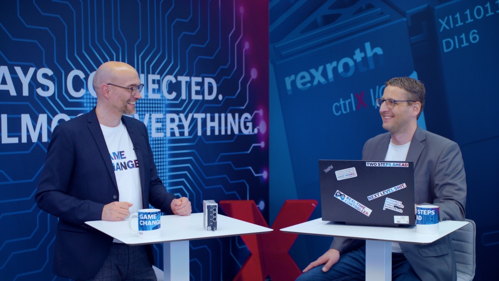 Gastgeber Christian Zentraf und sein Gast Kai Müller stehen an Besprechungstischen und sprechen über das Konfigurieren einer Handling-Applikation mit der ctrlX CORE, der Steuerungshardware der Automatisierungslösung ctrlX AUTOMATION